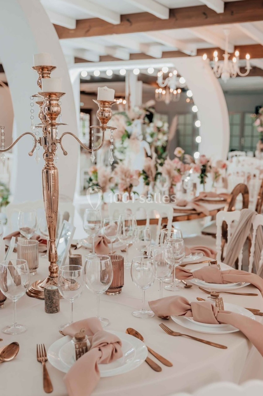 DOMAINE LE COMTE - jusque 200 personnes Salle de réception élégante avec tables décorées de nappes blanches, chandeliers dorés et serviettes roses.