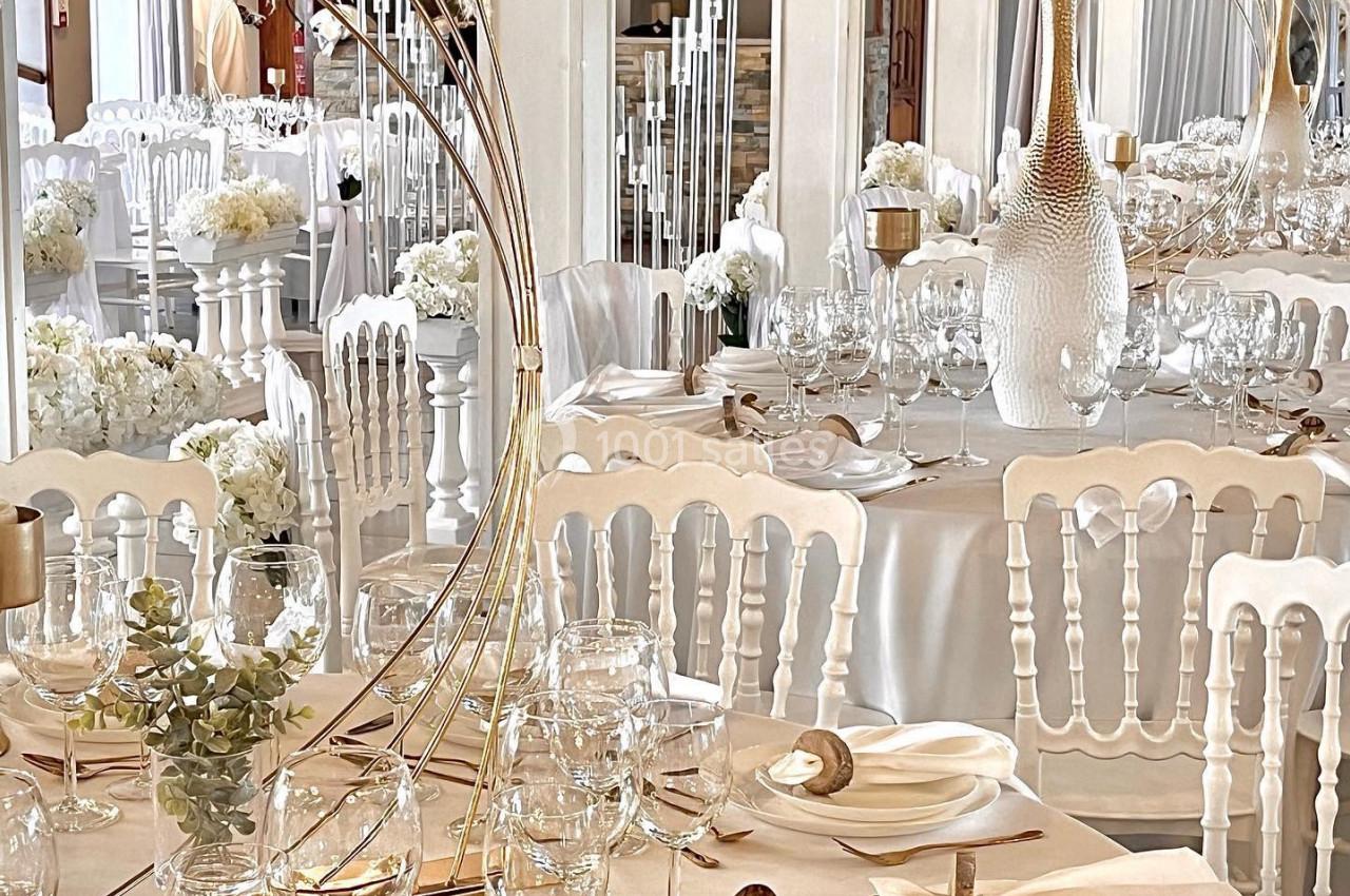 Tables élégamment dressées avec nappes blanches, couverts dorés, verres et décorations florales dans une salle de réception.
