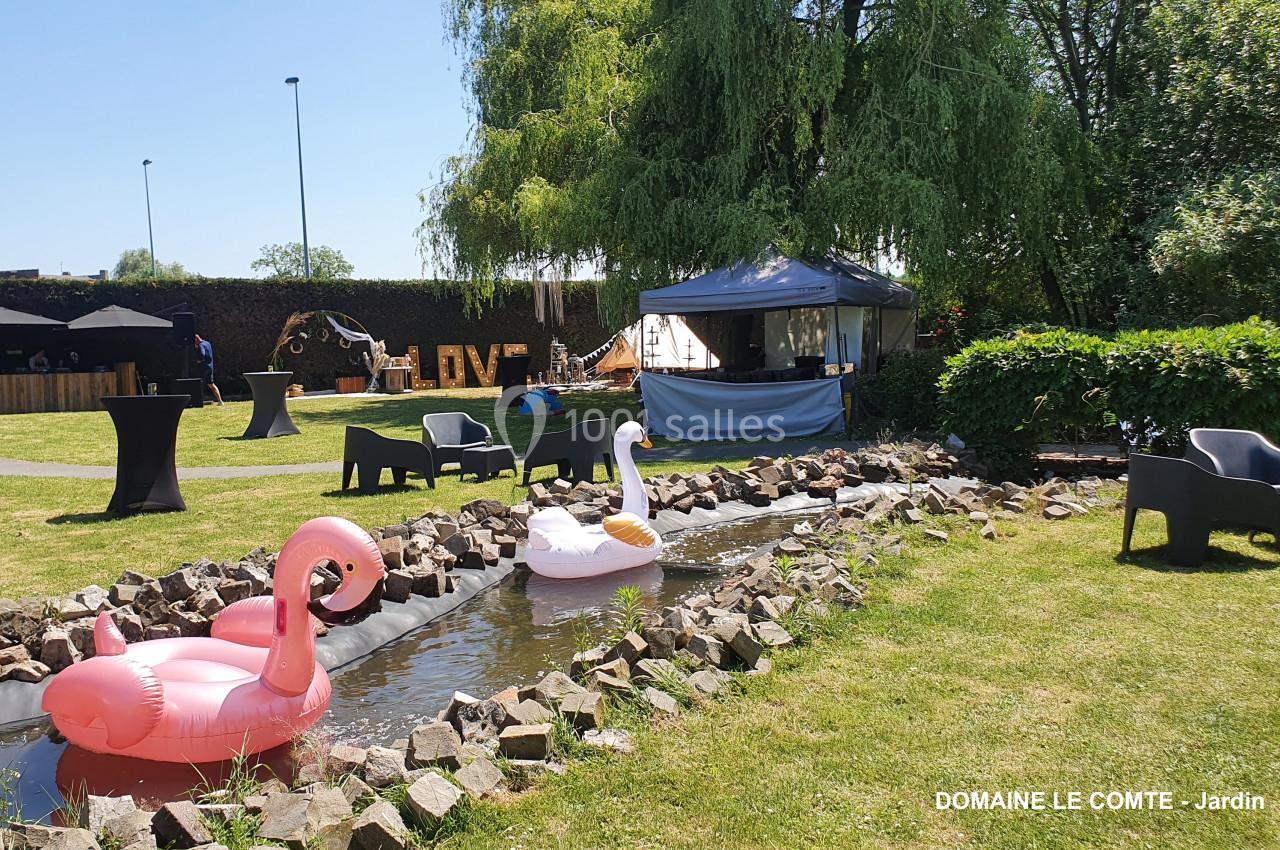Des bouées flamant rose et cygne flottent sur un ruisseau dans un jardin avec tonnelles et mobilier extérieur.