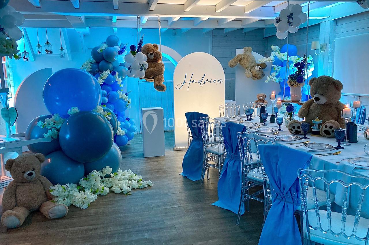 Décoration de salle avec ballons bleus, peluches d'ours et table dressée pour un événement festif.
