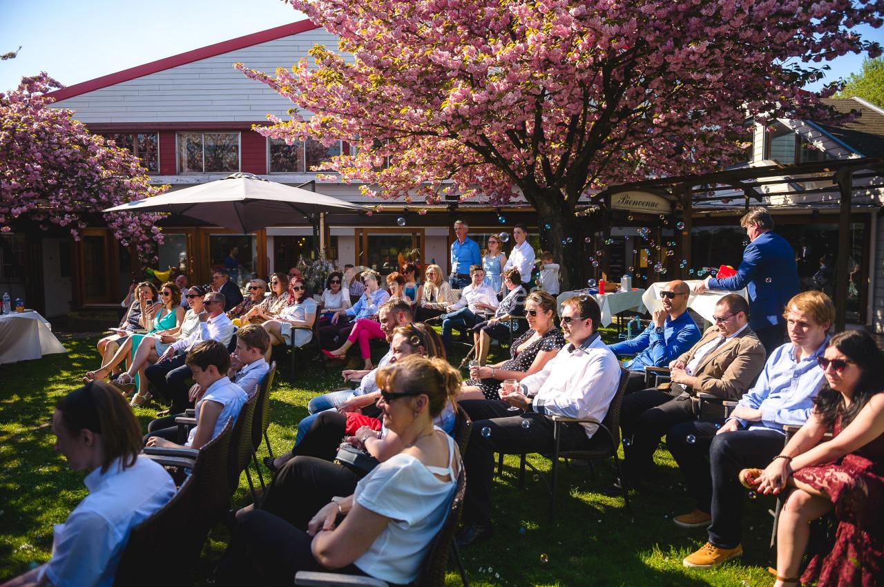 Groupe de personnes assises dans un jardin sous des cerisiers en fleurs, lors d'un événement en plein air.