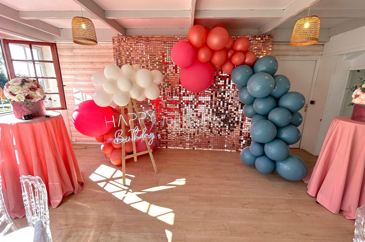 SALLE COSY - 30 PERS - Location à la journée 8h-18h Décoration d'anniversaire avec ballons colorés, mur scintillant, panneau ’Happy Birthday’ et tables drapées de tissu rose.