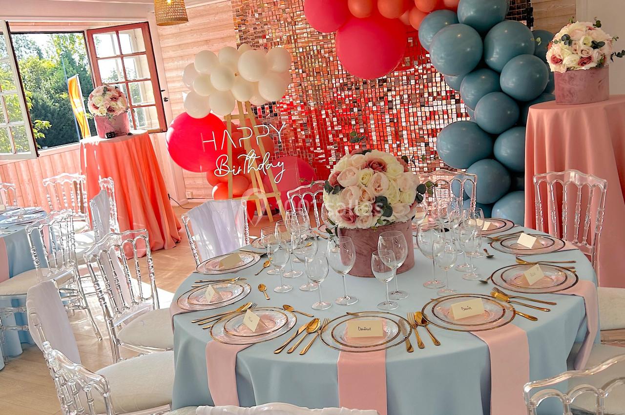 SALLE COSY - 80 PERS - Location à la journée 8h-18h Salle décorée pour une fête avec des tables dressées, des ballons colorés et un mur scintillant en arrière-plan.