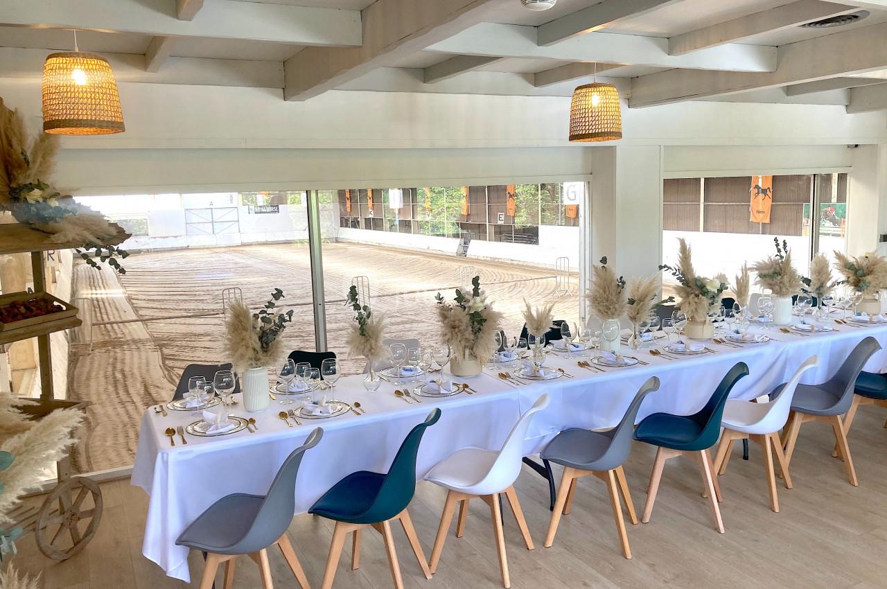SALLE COSY - 80 PERS - Location à la journée 8h-18h Salle lumineuse avec une longue table dressée, décorée de fleurs séchées, donnant sur une carrière équestre.