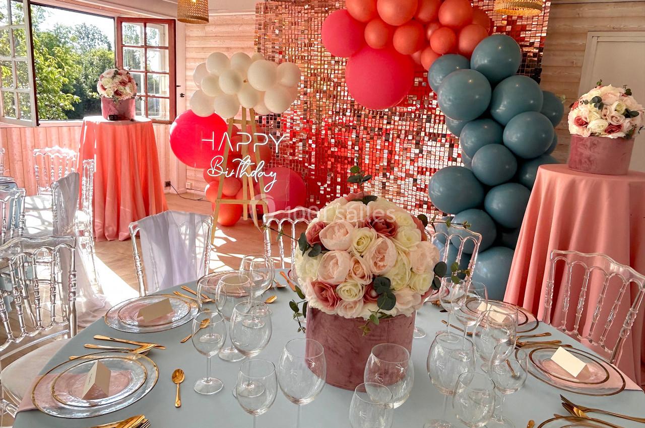 SALLE COSY - 80 PERS - Location à la journée 8h-18h Salle décorée pour une fête avec ballons colorés, tables dressées et bouquets de fleurs au centre.