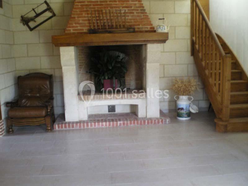 Cheminée en briques et pierre dans un salon rustique avec fauteuil, escalier en bois et décoration champêtre.