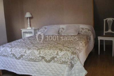 Lit double avec couvre-lit blanc, deux oreillers, table de chevet avec lampe rose et décoration florale sur les murs.