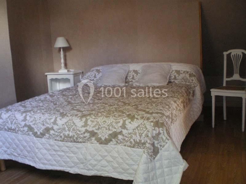 Lit double avec couvre-lit à motifs, deux oreillers blancs, une table de chevet avec lampe et une chaise en bois.