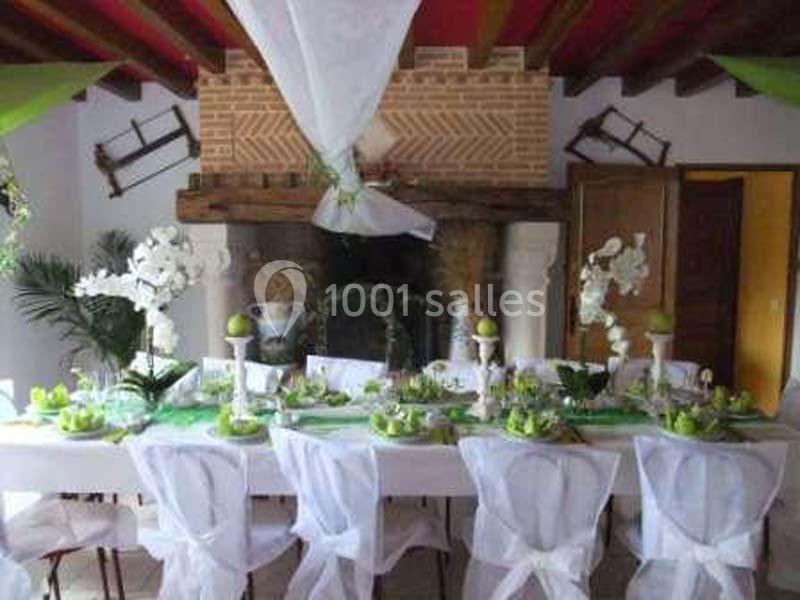 Table décorée pour un événement, ornée de nappes blanches, fleurs blanches et éléments verts, dans une salle rustique.
