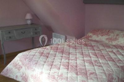 Lit double avec couvre-lit blanc, deux oreillers, table de chevet avec lampe rose et décoration florale sur les murs.