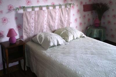 Lit double avec couvre-lit blanc, deux oreillers, table de chevet avec lampe rose et décoration florale sur les murs.