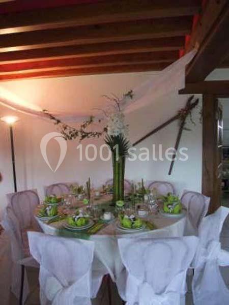 Table ronde décorée pour un événement, avec nappes blanches, serviettes vertes et centre de table floral, dans une salle…
