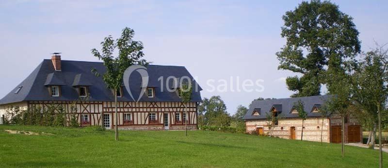 Maison à colombages et dépendances en briques dans un paysage rural avec pelouse et arbres.