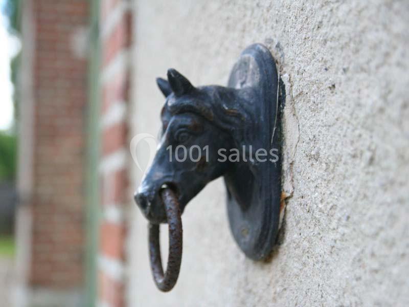 Anneau de fer fixé à une tête de cheval en métal sculpté, monté sur un mur en pierre.
