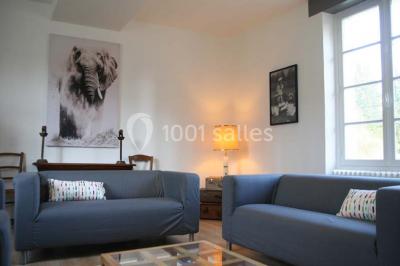 Deux canapés gris dans un salon lumineux avec une grande fenêtre, une lampe allumée et des décorations murales.