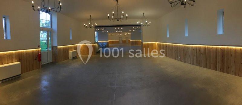 Salle spacieuse avec murs en bois, sol en béton et lustres suspendus, éclairée par des fenêtres et des lumières chaudes.