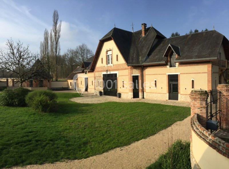 Bâtiment en briques avec toit en ardoise, entouré de pelouse et d'arbres, sous un ciel dégagé.