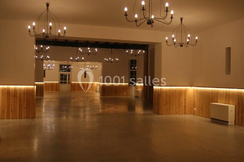 Salle vide avec sol en béton, murs en bois clair, éclairée par des lustres suspendus et des appliques murales.