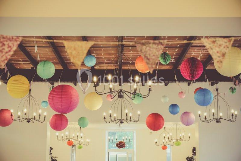 Guirlandes de fanions et lanternes colorées suspendues à un plafond avec des lustres dans une salle lumineuse.