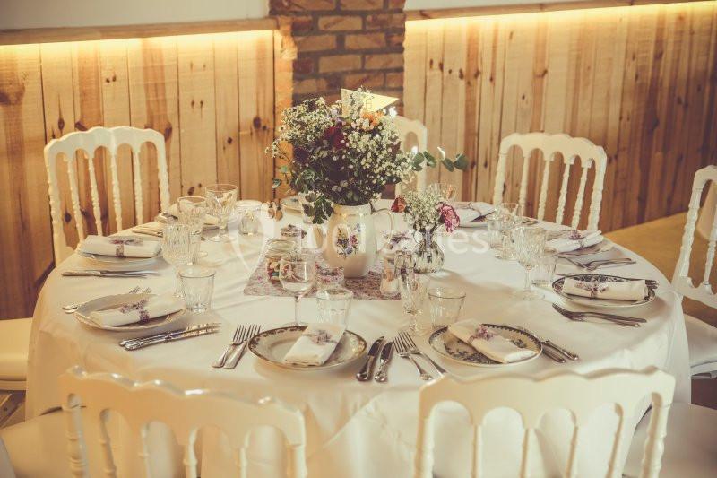 Table ronde élégamment dressée avec une nappe blanche, des couverts, des verres et un bouquet de fleurs au centre.