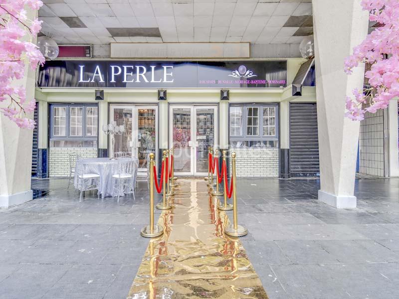 Entrée d'un établissement avec tapis doré, cordons rouges et décorations florales roses encadrant l'accès.