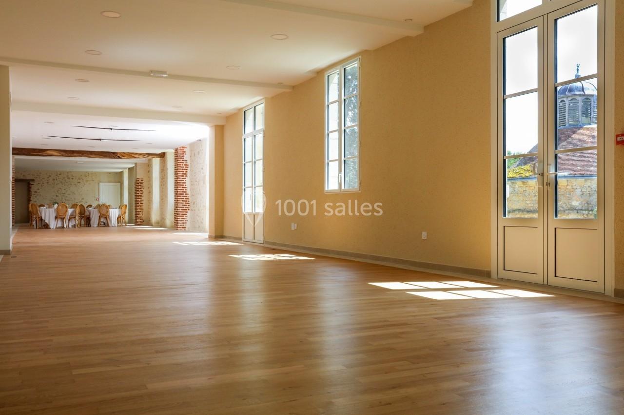 Salle lumineuse avec parquet en bois clair, grandes fenêtres et vue sur un clocher à l'extérieur.