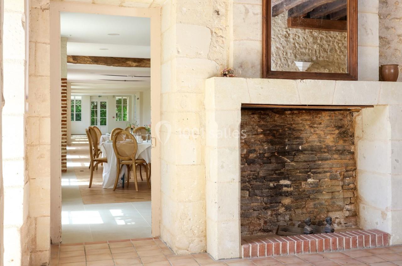 Cheminée en pierre dans une pièce lumineuse avec vue sur une salle à manger décorée de chaises et tables.