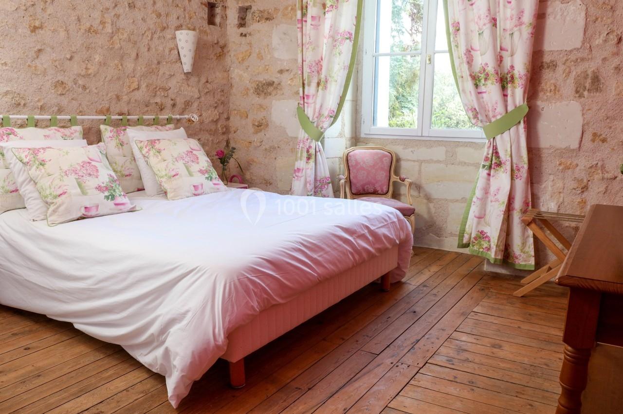 Chambre lumineuse avec un lit double, des murs en pierre, des rideaux fleuris et un parquet en bois.