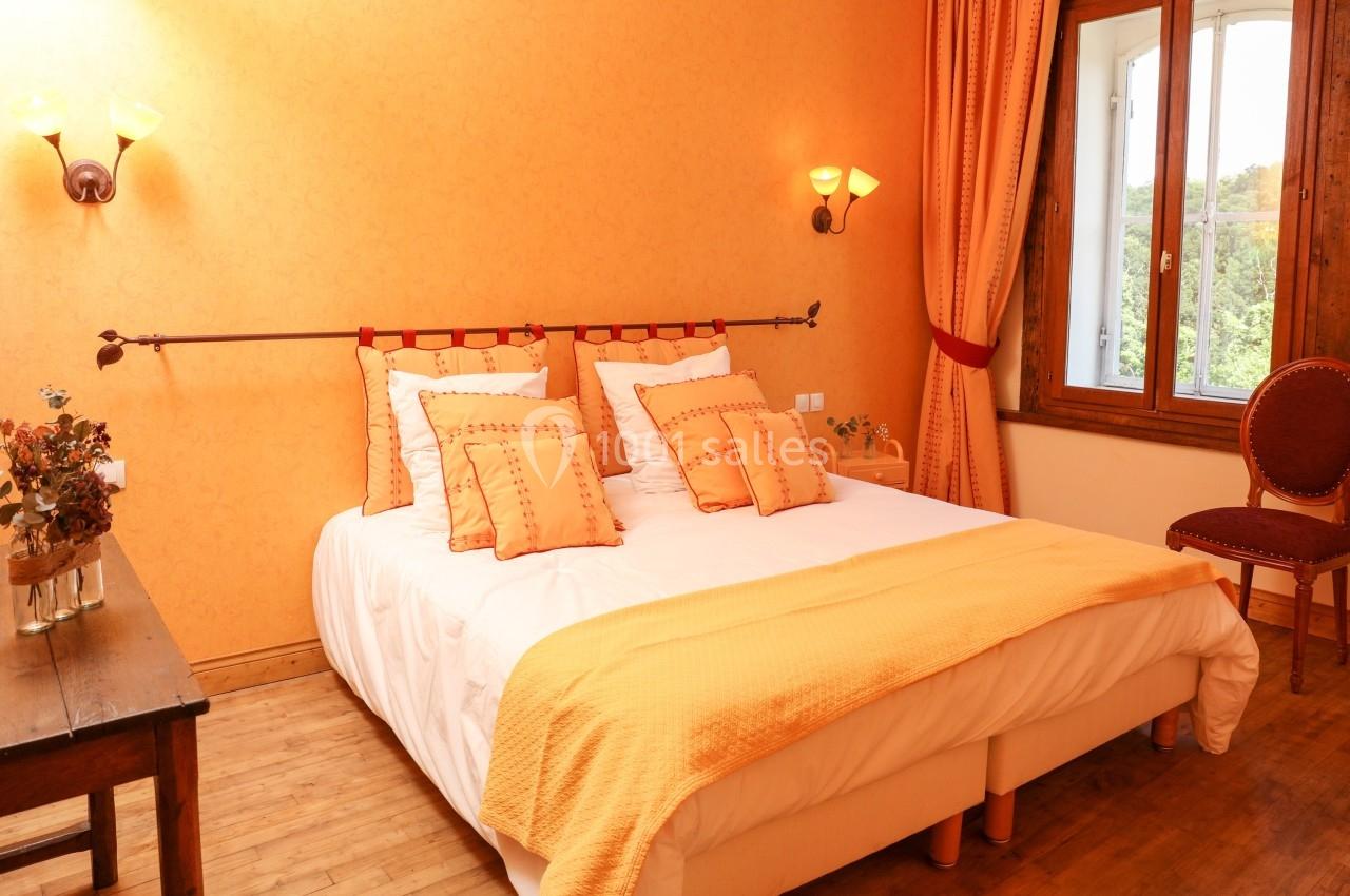 Chambre lumineuse avec lit double, couvre-lit orange, murs assortis, table en bois et fenêtre donnant sur l'extérieur.