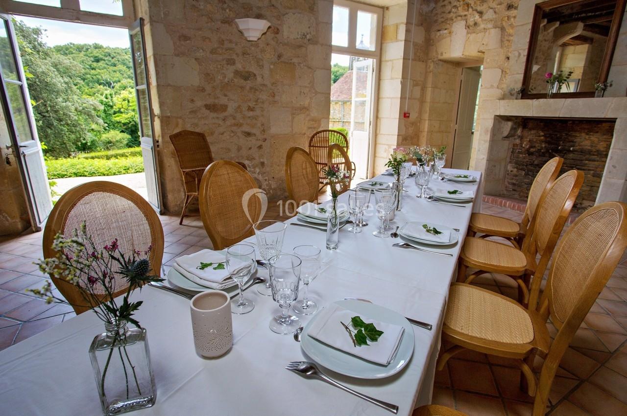 Table dressée avec vaisselle blanche et décoration florale dans une salle en pierre avec vue sur un jardin verdoyant.