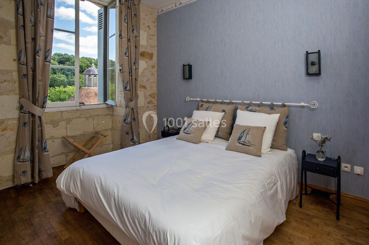 Chambre lumineuse avec un lit double, des coussins décorés de voiliers, et une fenêtre ouverte sur un paysage verdoyant.