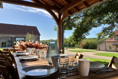 Terrasse en bois avec mobilier de jardin, offrant une vue dégagée sur un paysage verdoyant et boisé.