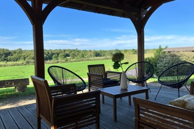 Terrasse en bois avec mobilier de jardin, offrant une vue dégagée sur un paysage verdoyant et boisé.