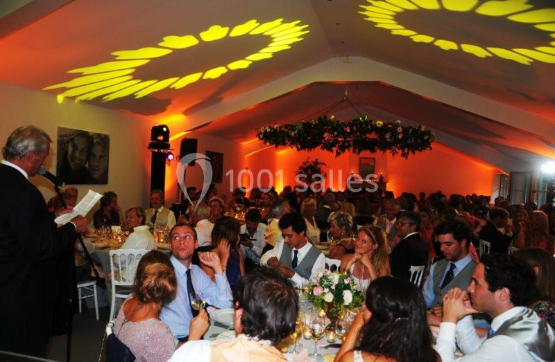 Salle de réception décorée, avec des invités assis à des tables, écoutant un discours lors d'un événement festif.