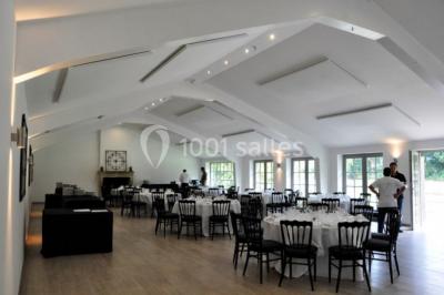 Salle de réunion lumineuse sous combles avec poutres apparentes, tables, chaises et écran de projection installé.