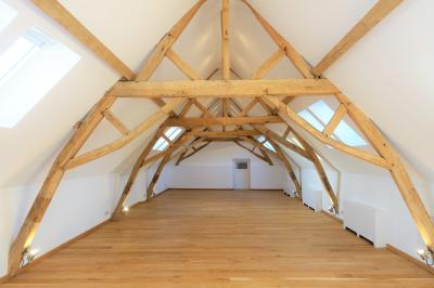 Salle de réunion lumineuse sous combles avec poutres apparentes, tables, chaises et écran de projection installé.