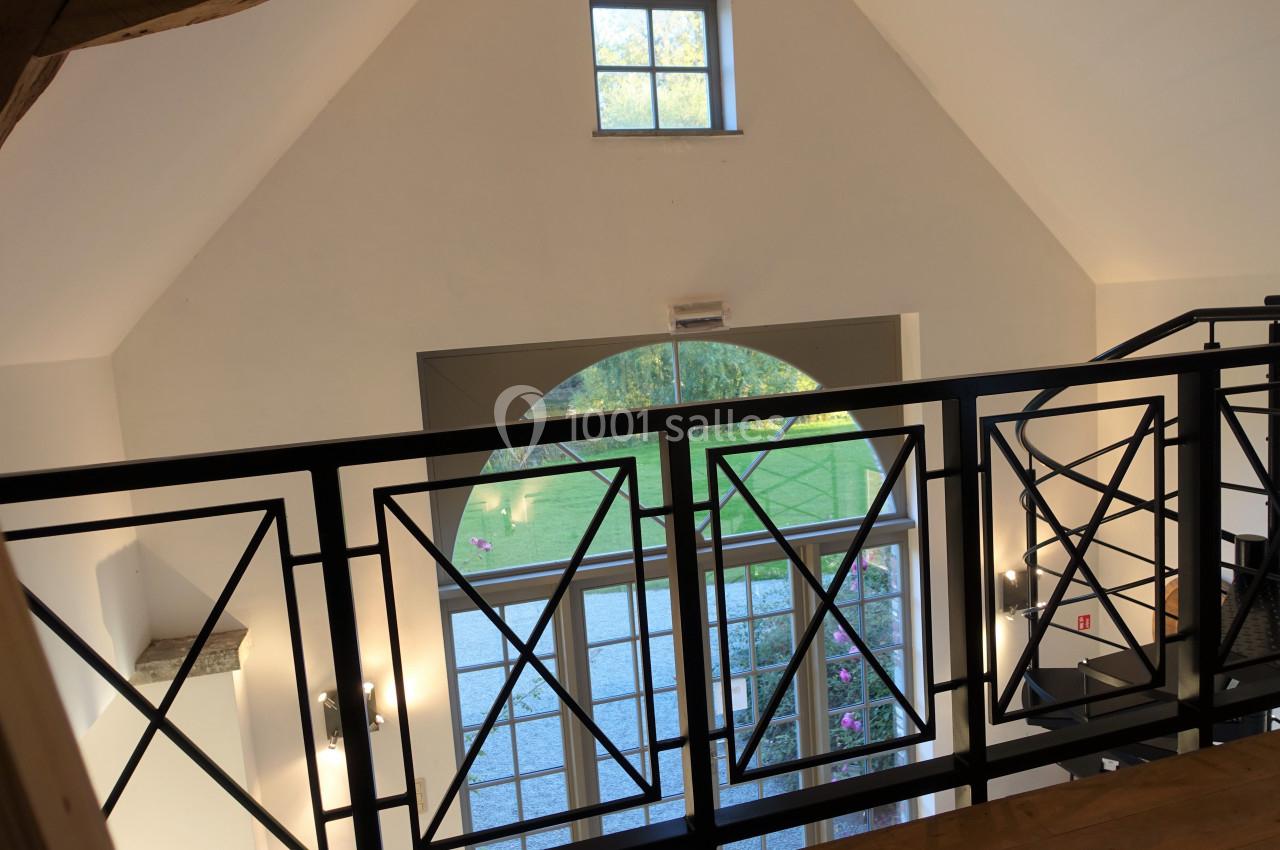 Vue intérieure d'une mezzanine avec garde-corps en métal, donnant sur une grande baie vitrée et un jardin extérieur.