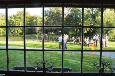 Vue d'un bâtiment en briques avec une tour, entouré d'arbres, d'une pelouse et d'un étang.