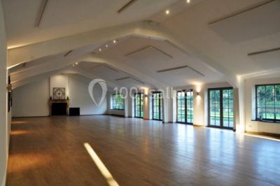 Vue d'un bâtiment en briques avec une tour, entouré d'arbres, d'une pelouse et d'un étang.