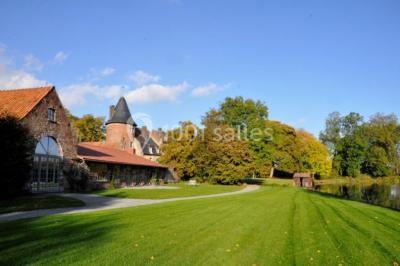 Vue d'un bâtiment en briques avec une tour, entouré d'arbres, d'une pelouse et d'un étang.