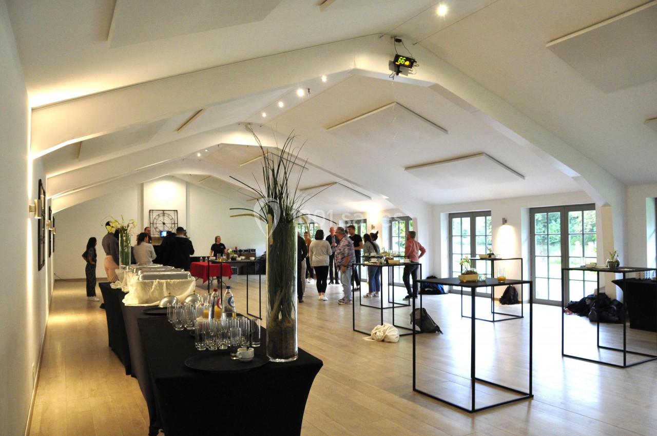 Salle lumineuse avec des tables dressées, des verres et des décorations, des personnes discutent en arrière-plan.