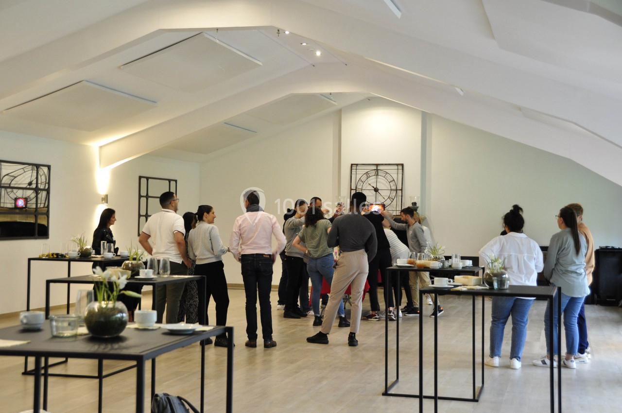 Un groupe de personnes debout dans une salle lumineuse, discutant près de tables décorées de fleurs et de vaisselle.