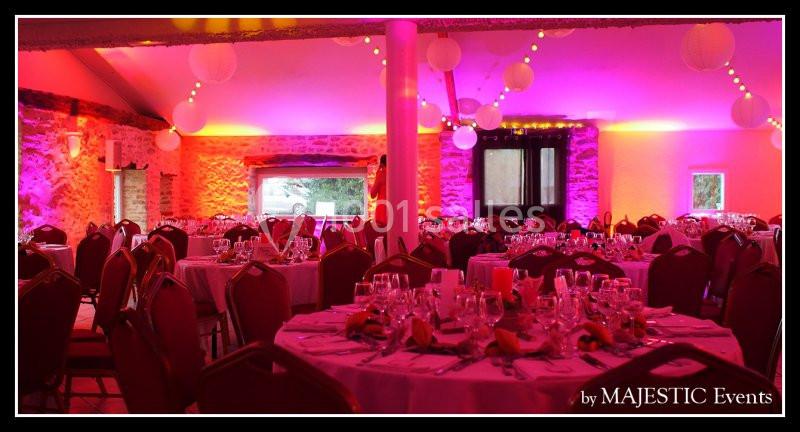 Salle de réception décorée avec des tables rondes dressées, éclairage rose et lanternes suspendues.