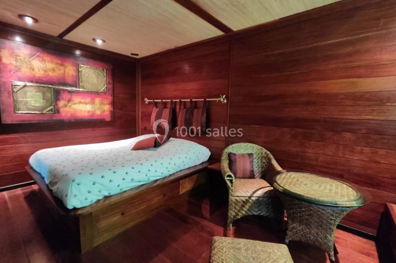 Chambre en bois avec lit double, décoration murale colorée, fauteuils en osier et petite table ronde.