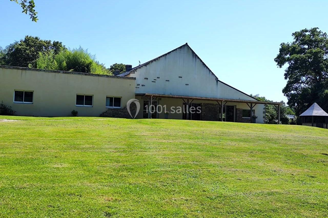 Bâtiment blanc avec toit en pente, entouré d'une pelouse verte et d'arbres sous un ciel dégagé.
