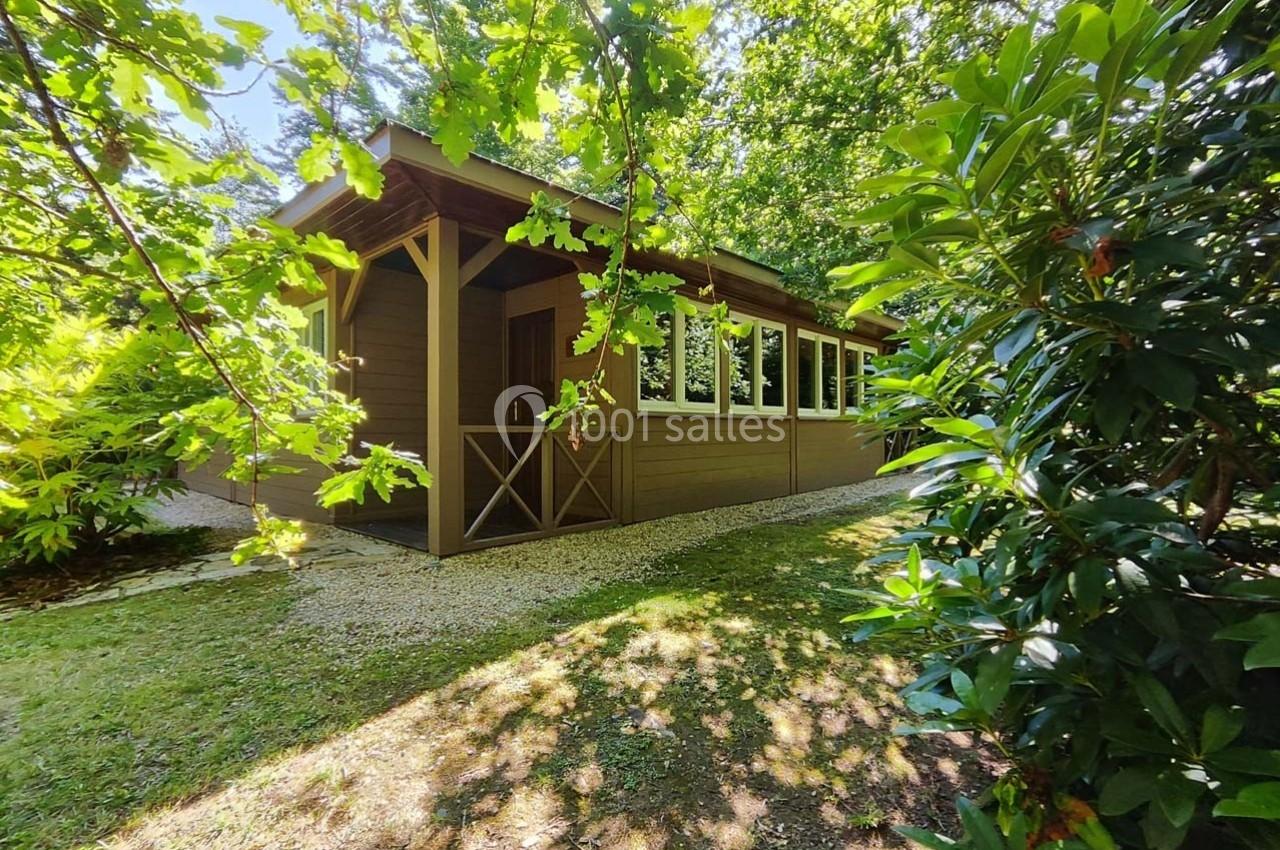 Chalet en bois entouré de végétation dense, avec un chemin de gravier à l'ombre des arbres.
