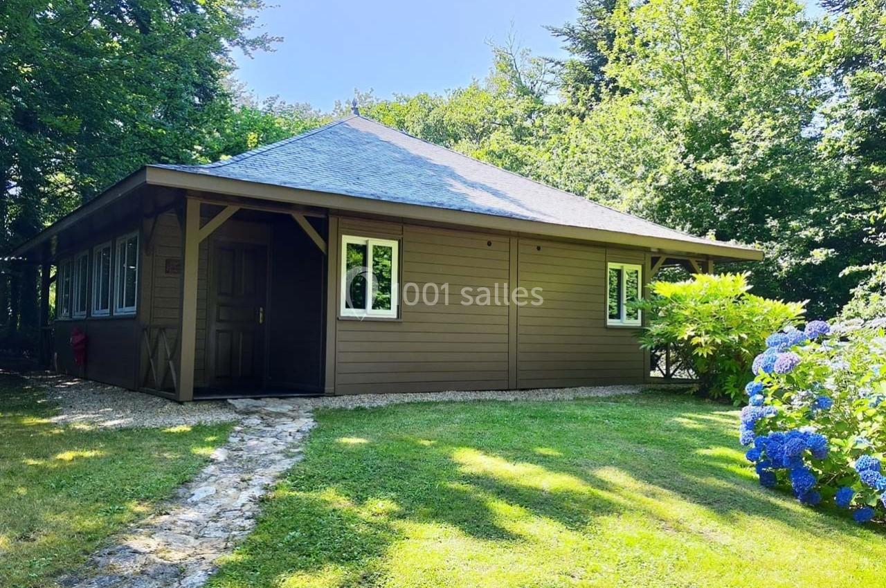 Chalet en bois avec toit en ardoise, entouré de verdure et hortensias, éclairé par une lumière estivale.