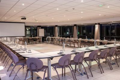 Salle de restaurant moderne avec une grande table en bois, suspensions noires et étagères de bouteilles illuminées.