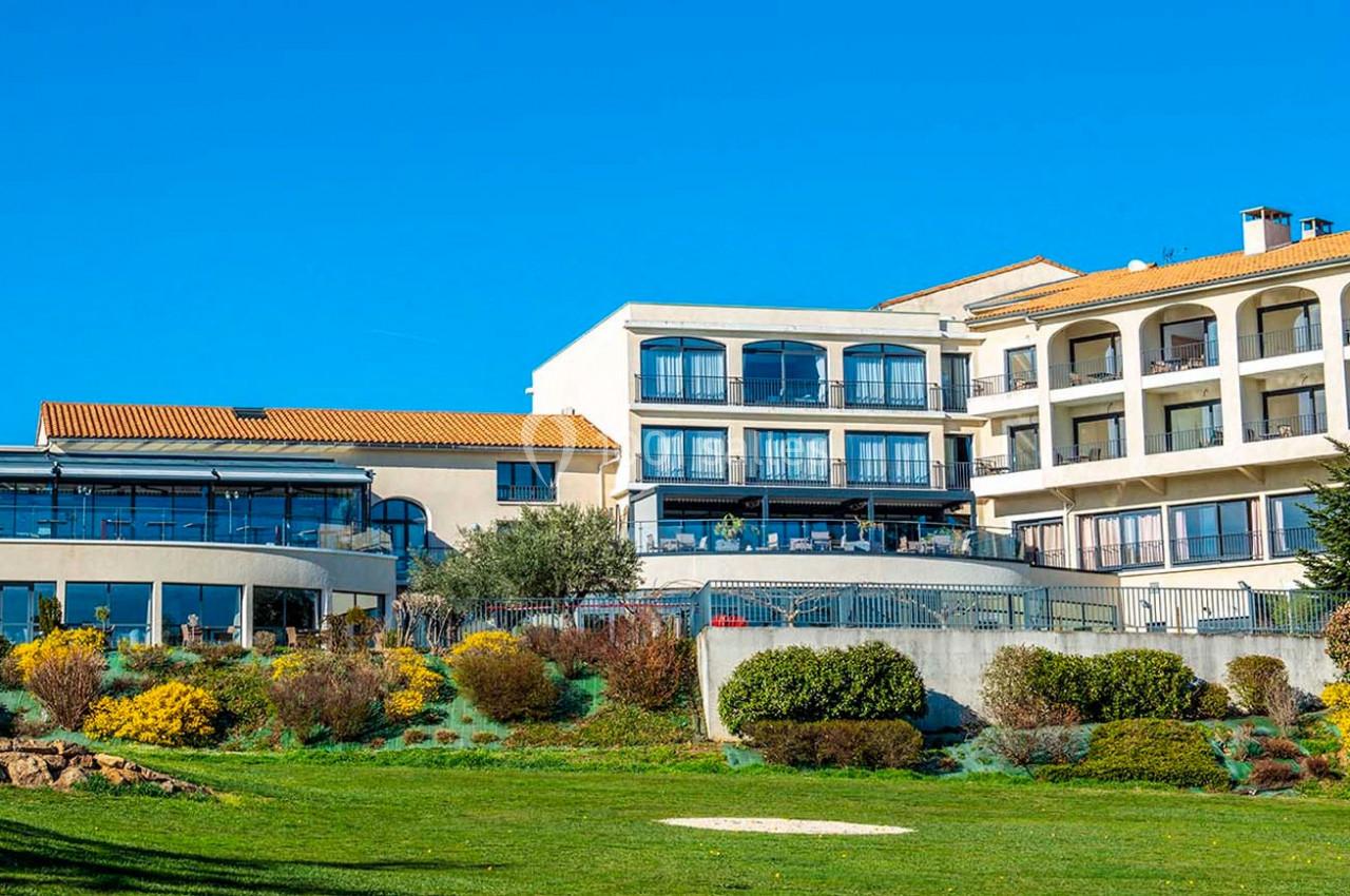 Bâtiment moderne avec façades blanches et toits en tuiles, entouré de jardins verdoyants sous un ciel bleu.