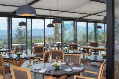 Salle de restaurant moderne avec une grande table en bois, suspensions noires et étagères de bouteilles illuminées.